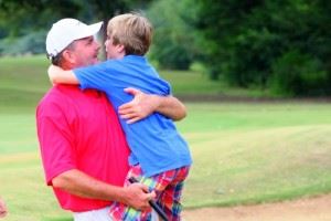 Gary Wigington gets a celebratory hug from 11-year-old son Peyton after winning the Calhoun County Championship Sunday. In the main photo, Wigington is congratulated by his playing partners after finishing off his winning 66 with an eagle on 18. (All photos by Greg McWilliams.) 