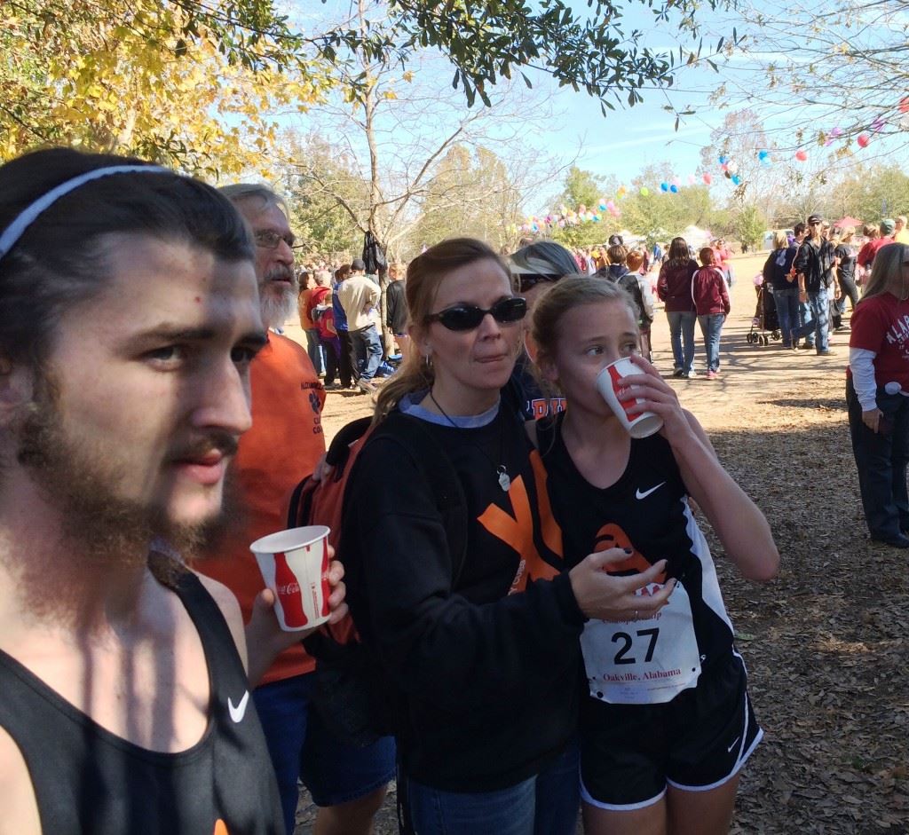 Alexandria's Abby Nunnelly (27) watches the finish of the Class 5A girls race unfold with her mother Amy. On the cover, Nunnelly gets support from a race aide after finishing second.