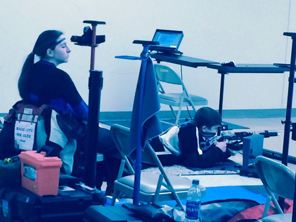 Anna Scheer (L) rests while Ryan McAndrews completes his prone relay at the CMP Alabama State Air Rifle Championships. Below, Alexis Poke secures her gun after finishing a winning Sporter program.