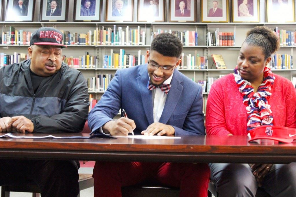 Donoho's Justin Foster, flanked by his parents Bobby and Shandal, signs his letter of intent with Samford Wednesday. On the cover, Foster is joined by family and friends after the signing. (Photos by Paige Faulkner)