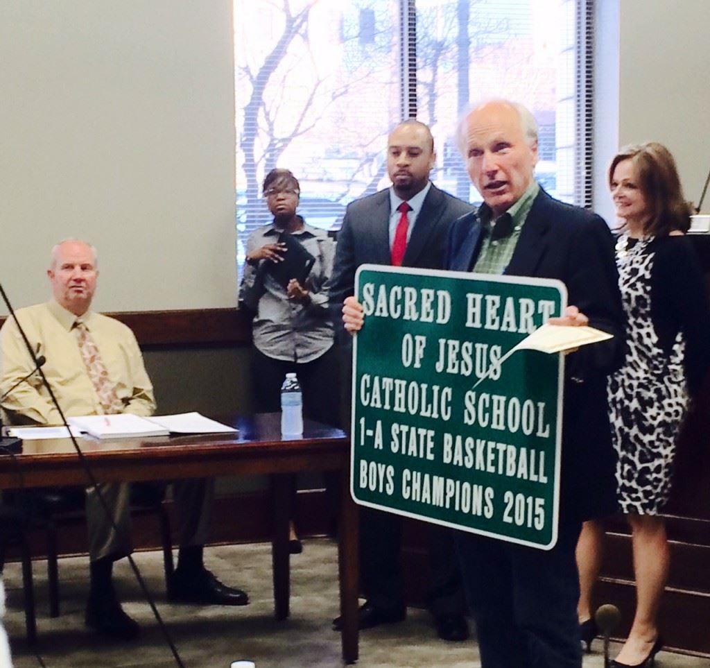 Anniston mayor Vaughn Stewart holds the road sign and a copy of the city resolution recognizing Sacred Heart's Class 1A boys basketball state championship. 