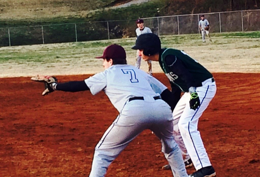 Donoho's Parker Morgan (7) holds Faith runner Grant Martin close at first base. On the cover, Donoho left-hander Brett Holmes looks in for a sign.