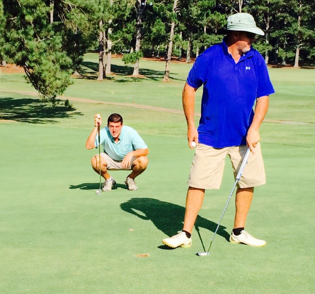 Dalton Chandler (L) lines up his putt on Pine Hill's 16th green as his father Ott moves off after completing the hole. 