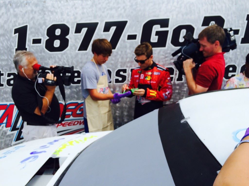 Sprint Cup driver Jamie McMurray (center right) preps White Plains Middle School student Jacob McCulley for applying a green hand print to an old Cup car during a promotional appearance at Talladega Superspeedway Tuesday.