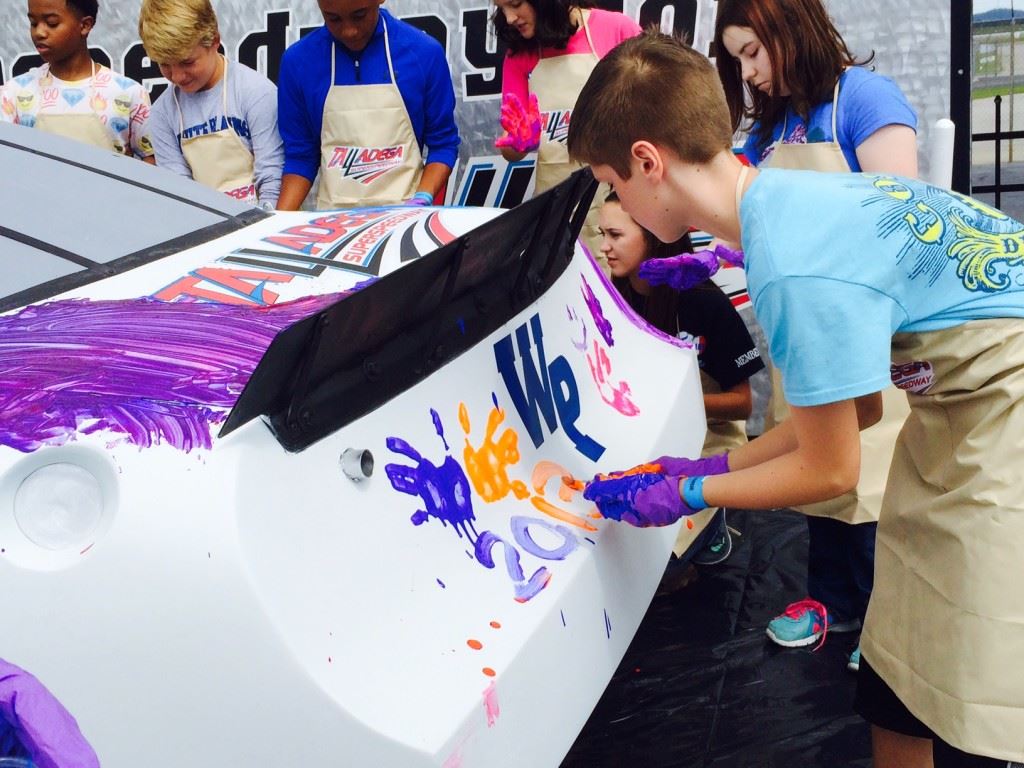 Payton Wilburn applies Auburn colors to the back of Jamie McMurray's car during a promotional visit to Talladega Superspeedway Tuesday. The colors were an homage to McMurray's 2013 win here in an Auburn-themed car.