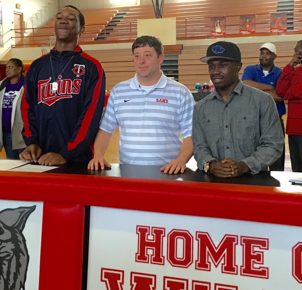 Saks coach Jonathan Miller is flanked by seniors DeMario Burnett (L) and Demetrius Powell after the players announced their post-high school playing intentions Wednesday. On the cover, Burnett awaits the start of the ceremony.