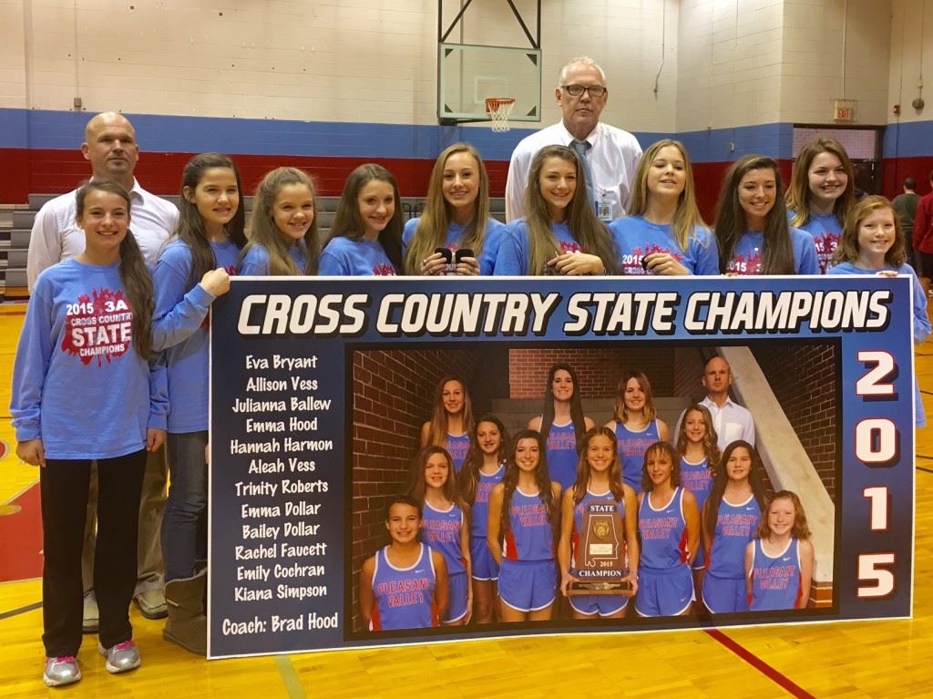 Pleasant Valley's state champion girls cross country team, along with coaches Brad Hood (L) and Rex McAllister, stand with the sign that will hang in the gym to commemorate their feat. On the cover, the team shows off its championship rings. (Cover photo by Emily Harrell)