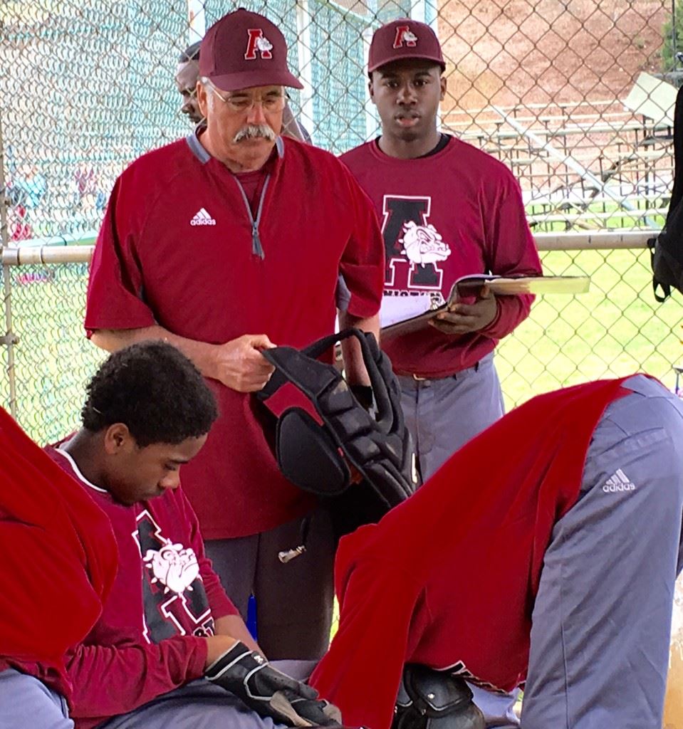 Anniston baseball coach Paul Farlow watches as catcher Jimmy Felton gets his gear on between innings. On the cover, the Bulldogs huddle to break down the day's game. 