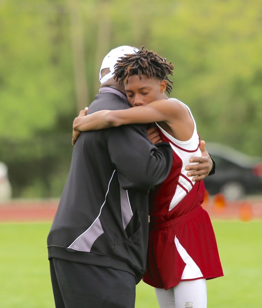 Anniston senior Leonard Brown embraces assistant coach Leroy Clark after an emotional run in Tuesday's Calhoun County Track Meet. On the cover, Leonard (R) and younger brother Nick dedicated their effort in the meet to the memory of their mother, who passed away earlier in the day. (Photo by Kristen Stringer/Krisp Pics Photography).