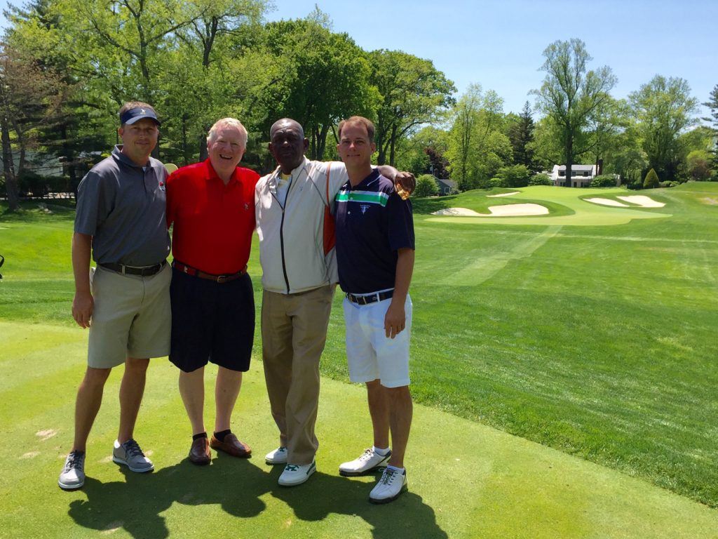 Matt Rogers (L), Jeremy McGatha (R) and their caddy Delroy pose with the owner of the house behind No. 10 green on the West Course at Winged Foot (background) that gave Byron Nelson a specific aiming point. 