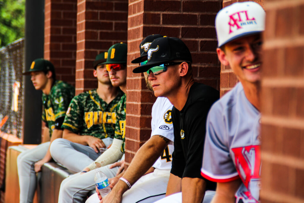 Choccolocco Monsters coach Dalton Cobb watches the action on the field from the National Stars’ dugout. Monsters’ Weston Kirk is seated beside him. (Photo by Isabella Martinez)