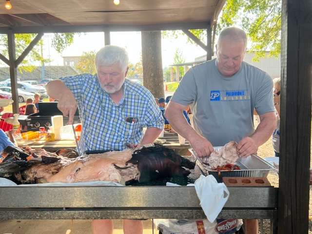 Piedmont Booster Club president Mike Pody (R) and Vernon Young carve up the pig they had prepared for the tailgaters before Thursday night’s game with Anniston.