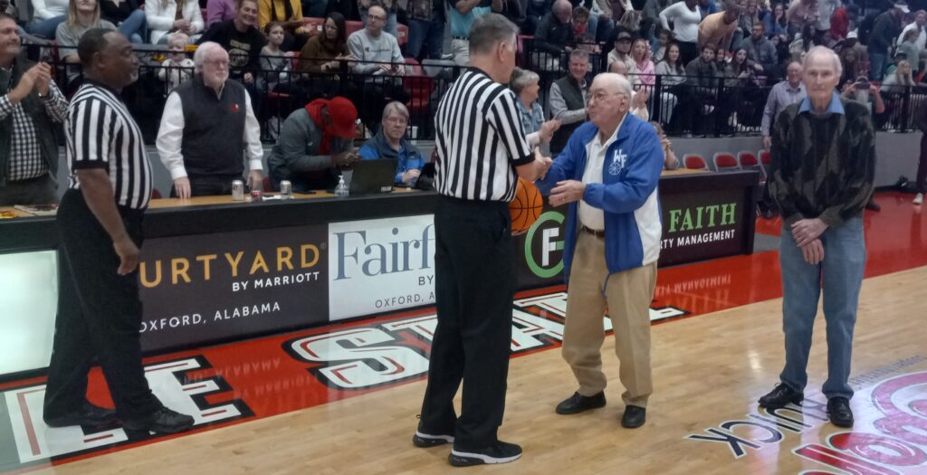 Former White Plains basketball player Alvin Robertson presents the game ball to officials as former teammate Charles Thornburg looks on before Friday’s boys Calhoun County championship game in Pete Mathews Coliseum. (Photo by Joe Medley)