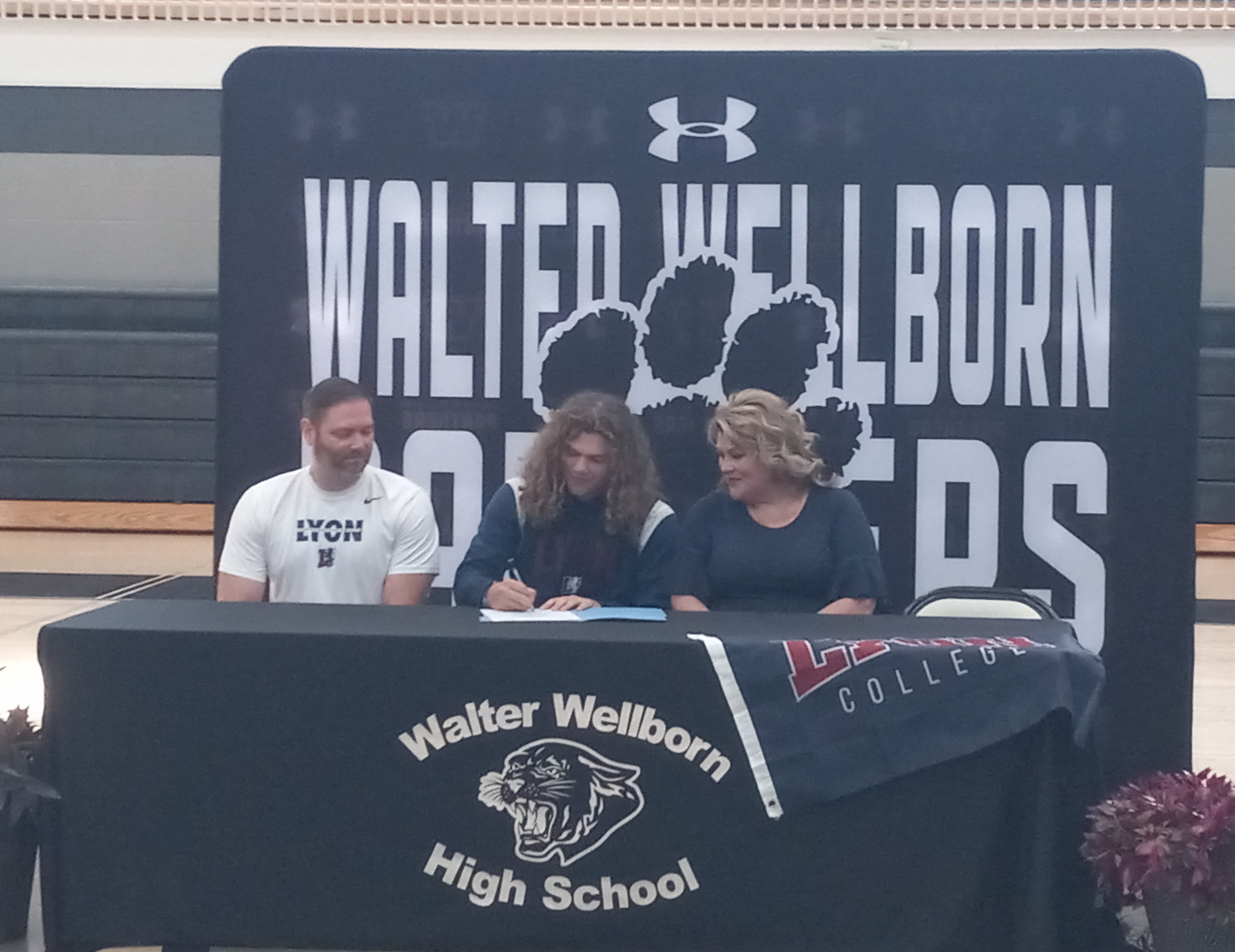 Wellborn quarterback Grayson Johnson signs to play for Lyon College as his parents, Todd and Shannon Johnson, look on Tuesday in Wellborn High School’s gymnasium. (Photo by Joe Medley)