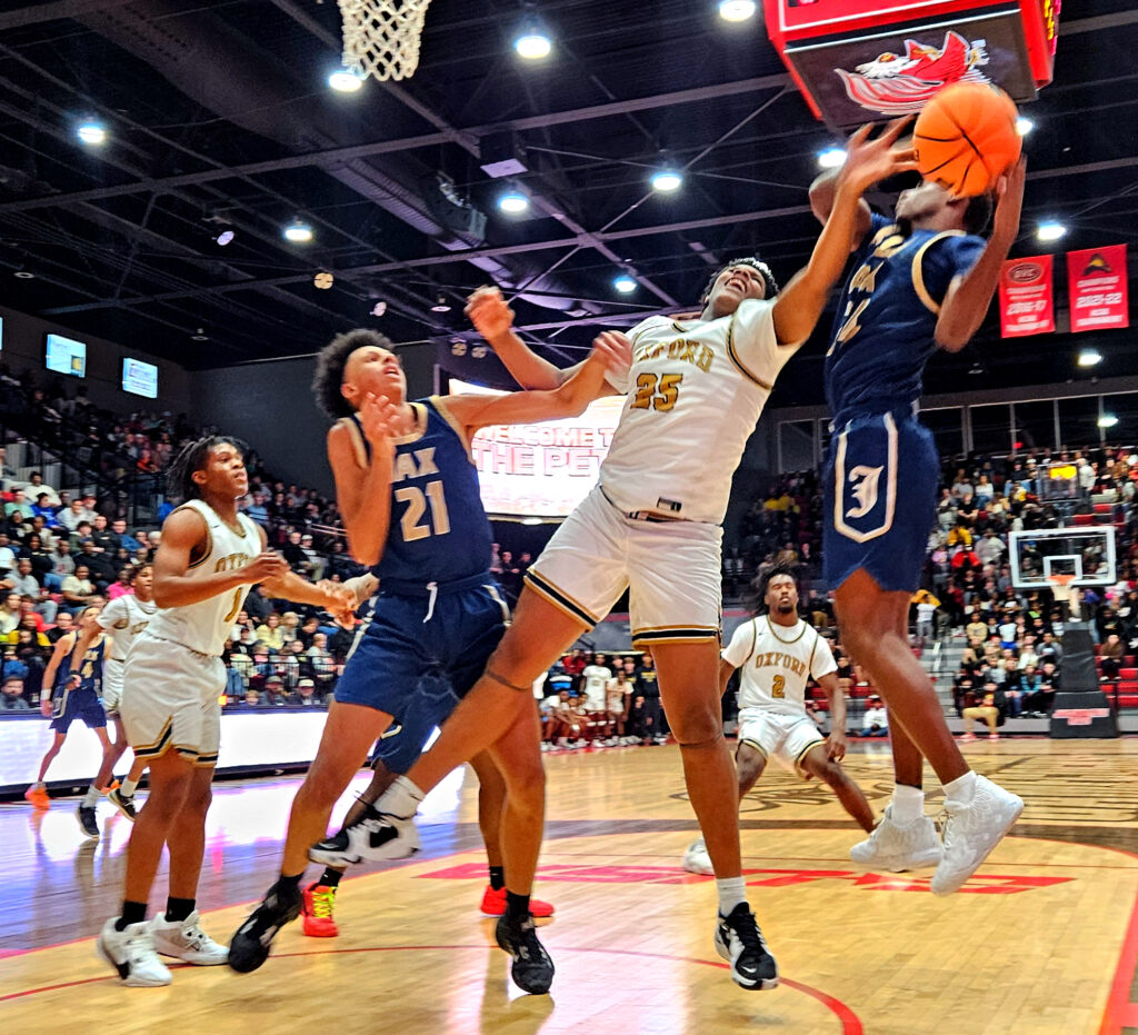 Oxford’s Anthony Bush (25), Jacksonville’s Sean Herbert (21) and Ky’dric Fisher battle for a rebound during Friday’s Calhoun County boys’ final in Pete Mathews Coliseum. (Photo by Joe Medley)