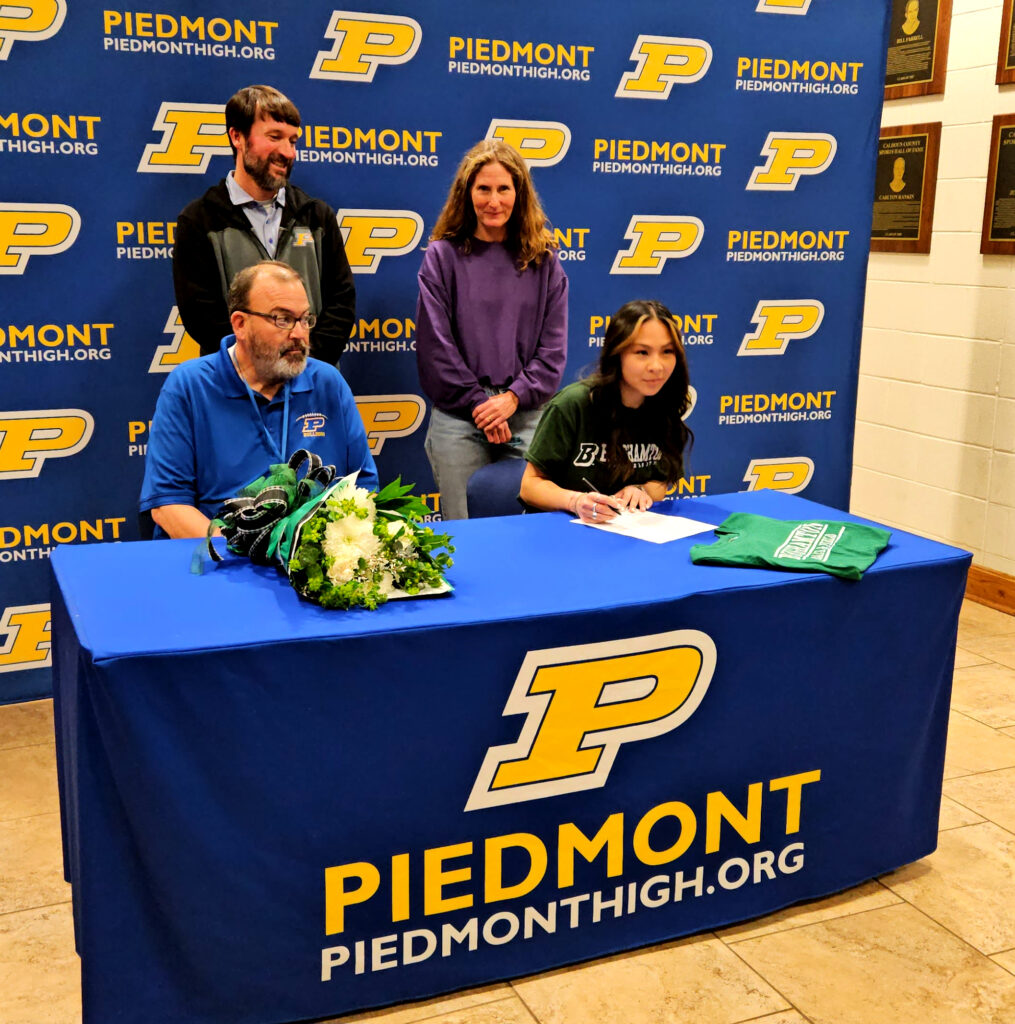 Piedmont’s Lexi Ray (seated, right) signs Monday as her Piedmont coaches look on. (Photo by Joe Medley)