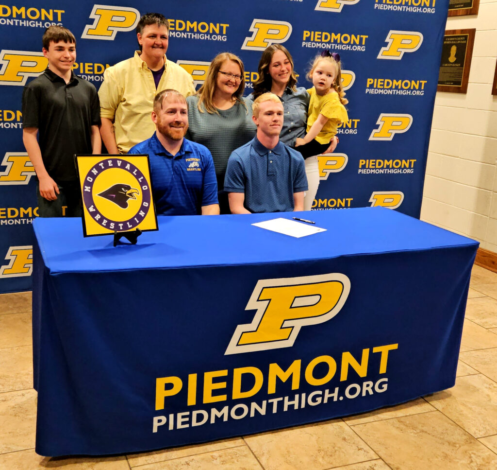 Piedmont’s Izak Bailey (seated, right) poses for pictures with his coach and family during Monday’s signing ceremony. (Photo by Joe Medley)