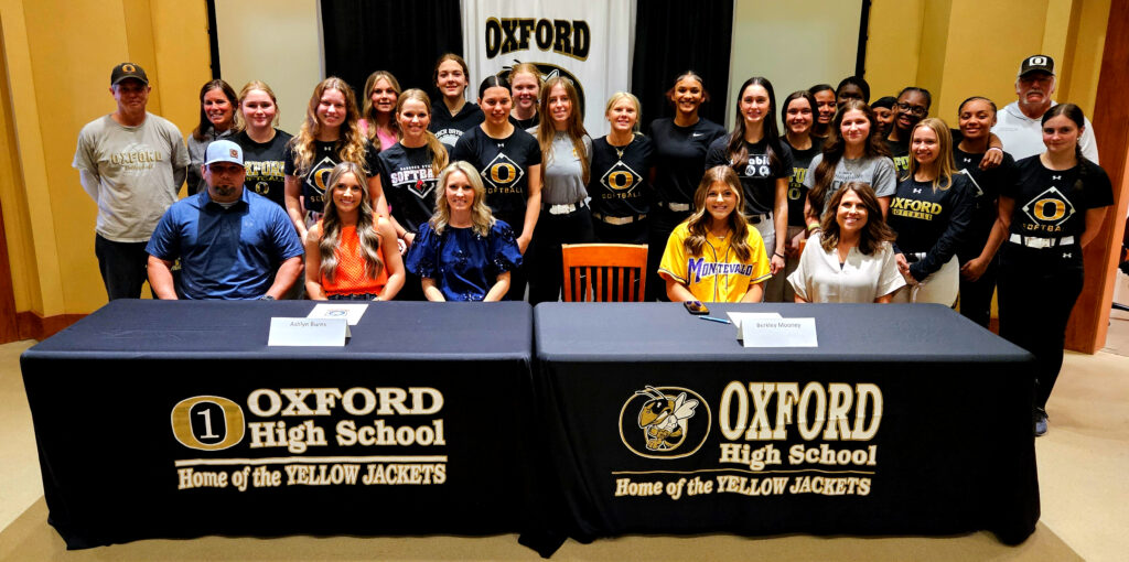 Oxford’s Ashlyn Burns (center left) and Berkley Mooney pose for a picture with Oxford softball coaches and teammates at Monday’s signing ceremony.