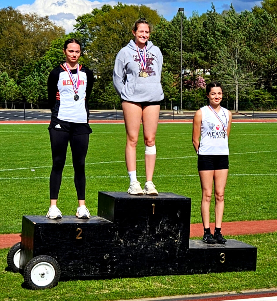 Donoho’s Estella Connell tops the high-jump podium Wednesday at Choccolocco Park. Alexandria’s Anna Beth Stewart (left) finished second and Weaver’s Jaylee Carter third.